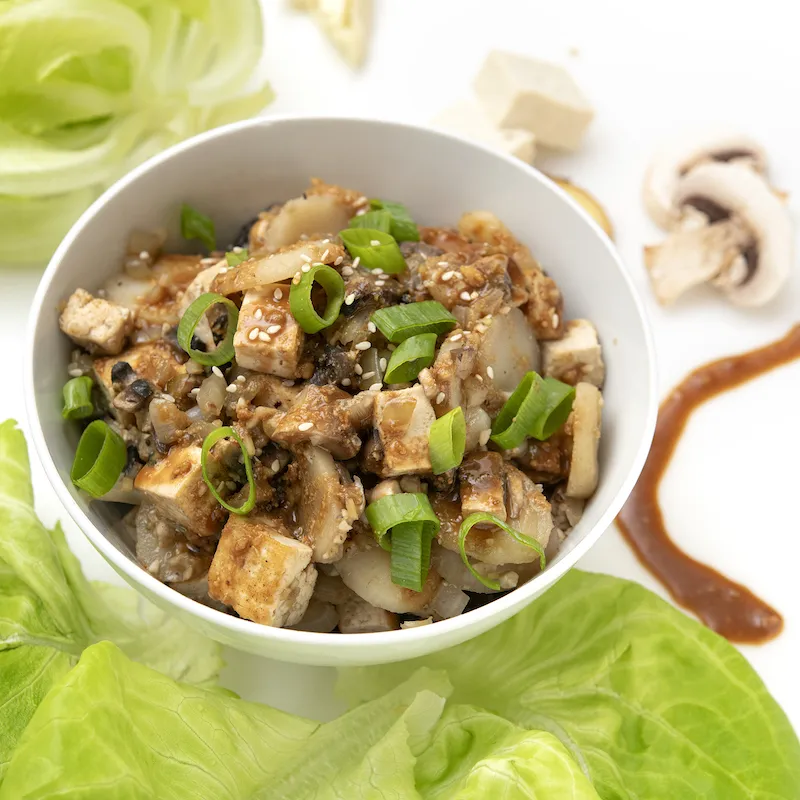 Bowl of tofu chunks and green onions with lettuce garnish