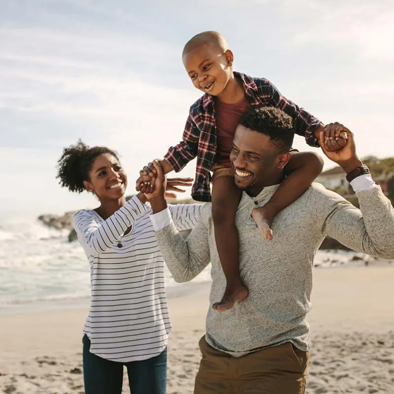 Mother and father walking on beach with son on father's shoulders