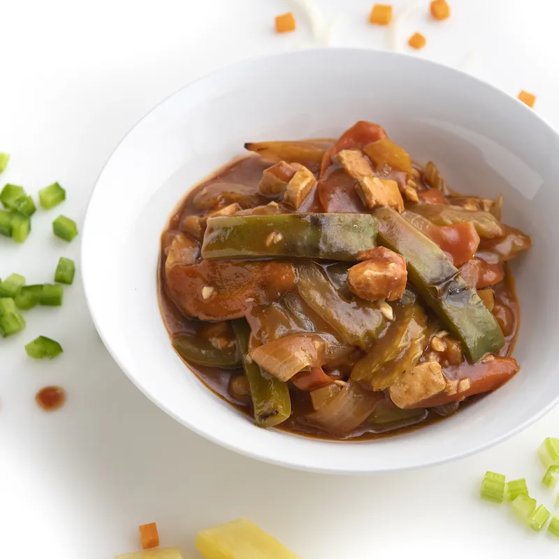 White bowl full of sweet and sour chick'n with chopped green pepper garnish on counter