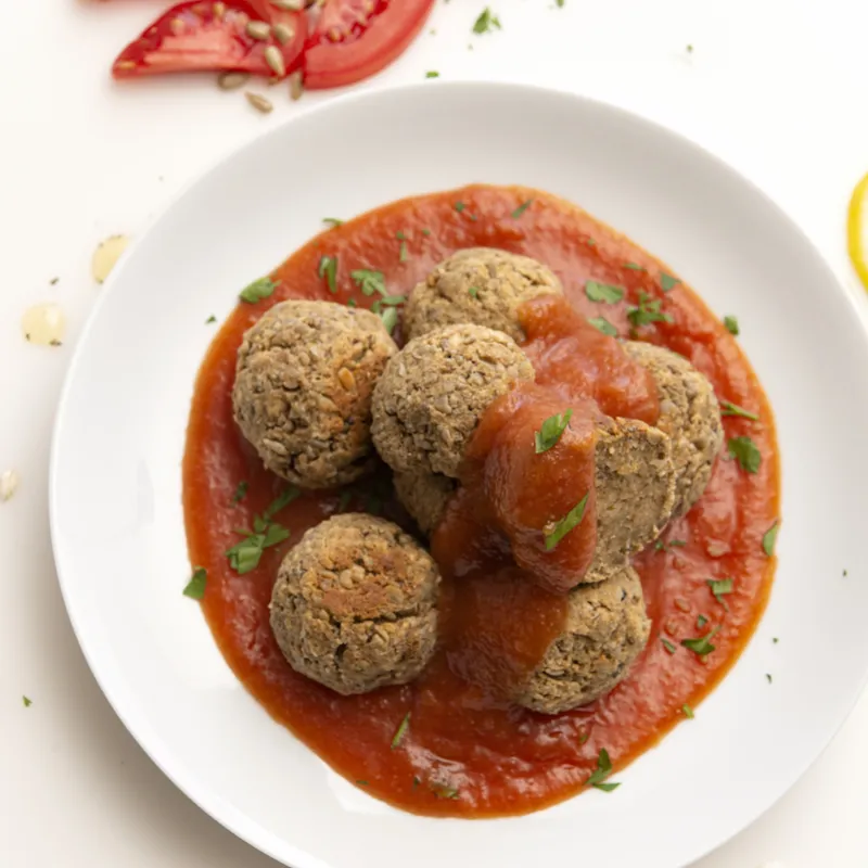 White bowl of tofu meatballs and sweet and sour sauce with lemon garnish