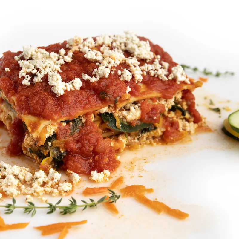 Square of lasagna on white counter with herb sprig garnish