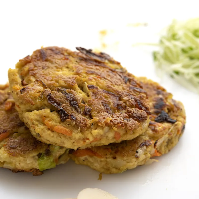 Three tofu yung patties on white surface with shredded zucchini garnish