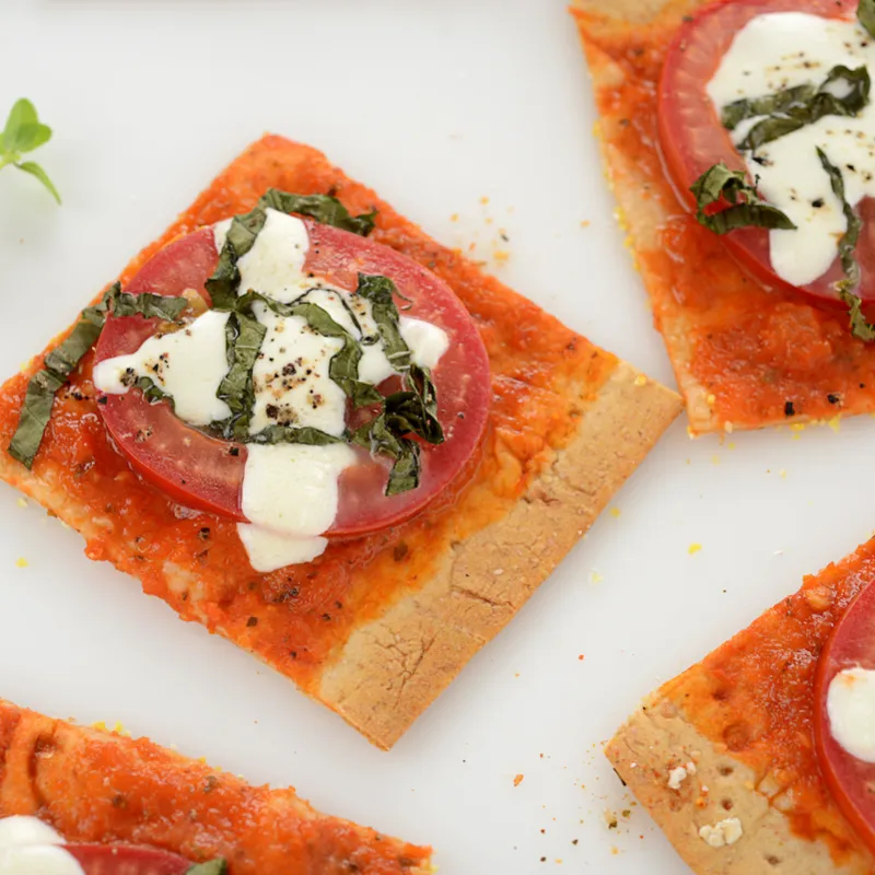 Four square pieces of margherita pizza with green garnish.