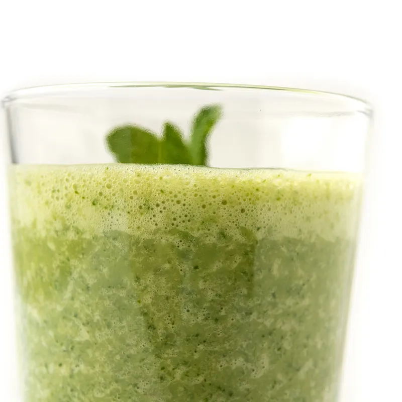 Clear glass of green smoothie with sprig on top