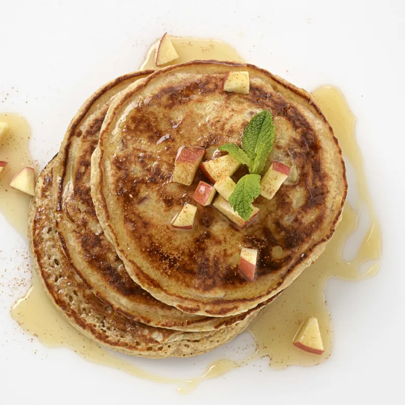 a stack of three homemade pancakes, topped with cubed apples