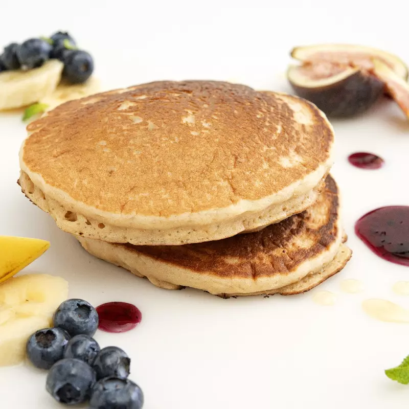 a short stack of pancakes, surrounded by fresh blueberries, banana slices and other fruit