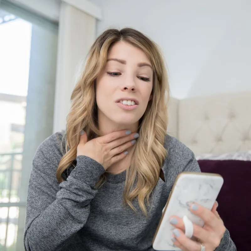 Woman holding throat while on phone