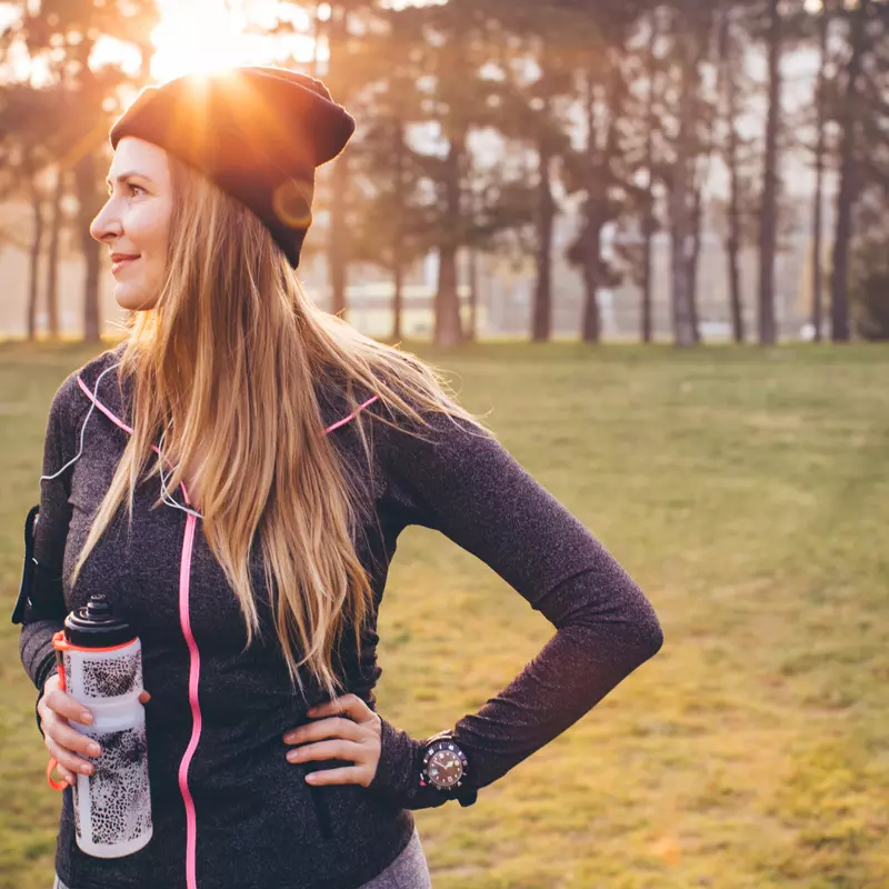 Woman wearing active wear and holding a water bottle in a park during winter.