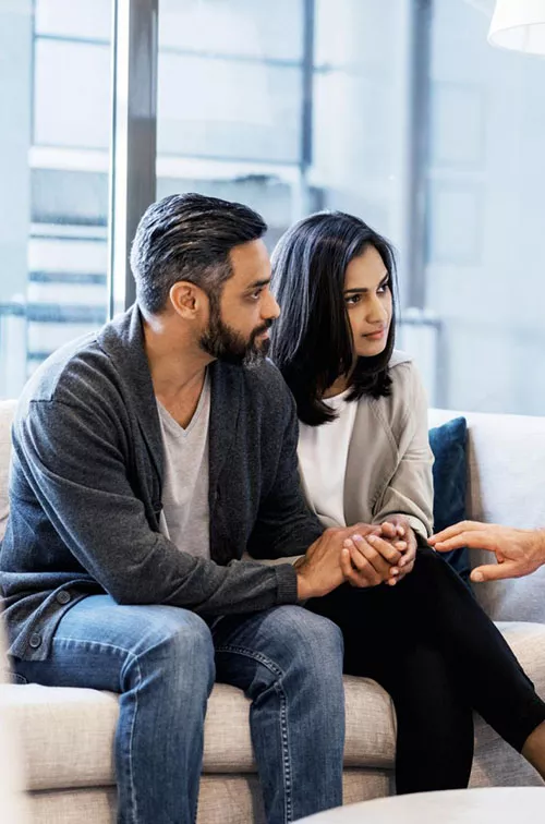 A couple, sitting with a doctor who is comforting them.