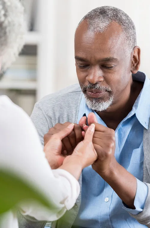 Elderly couple sitting across from each other, clasping hands, and praying together.