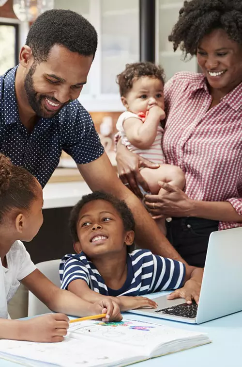 A family of five is in the kitchen, helping two of their children with their homework.