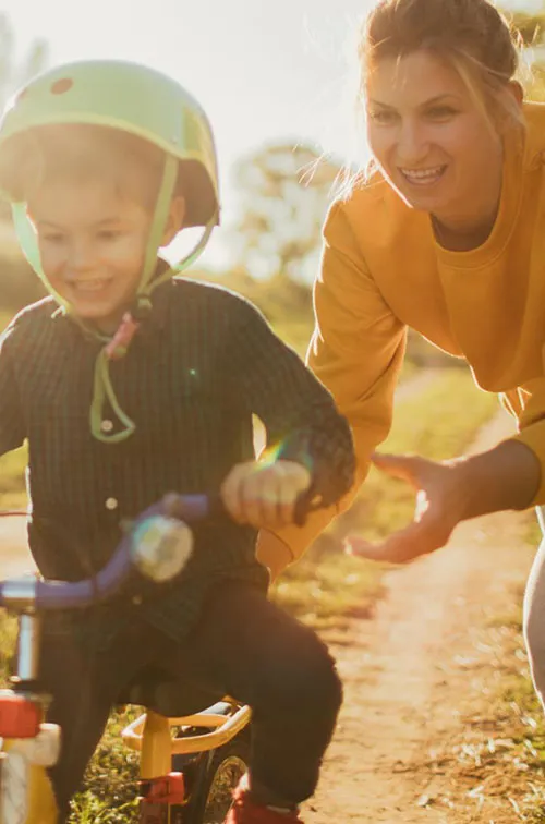 A mom pushes her son a bike, outside.