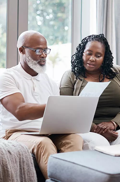 Man and woman reviewing paperwork with computer on lap