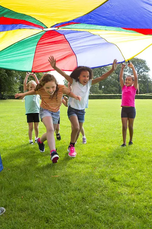 A group of children outside playing with a large multicolored parachute.