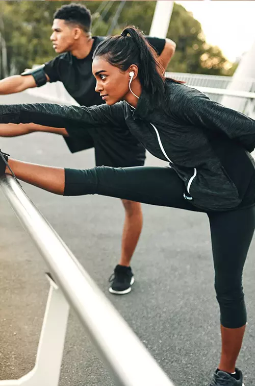 Two runners, stretching side by side, their legs extended and touching their toes.