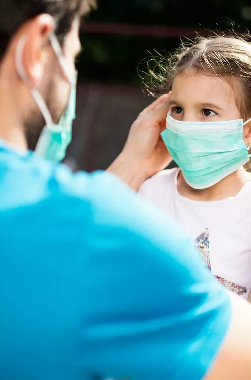 Father putting mask on daughter outdoors