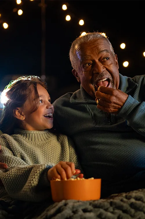 Grandfather watching a movie outdoors with his granddaughter.