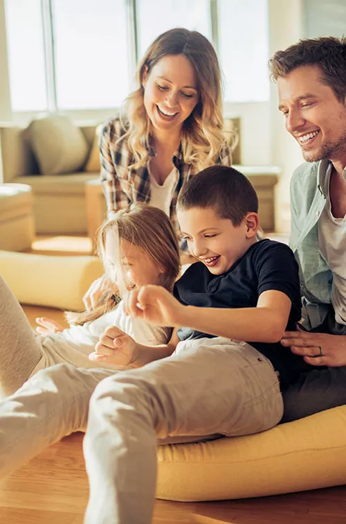 Family playing and laughing together in a sun filled living room of their house.