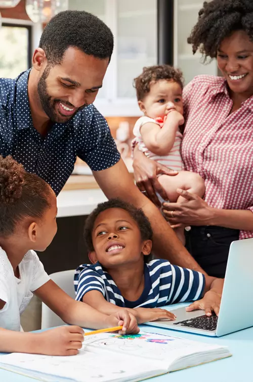 Photo of a family standing at a laptop making plans and smiling.