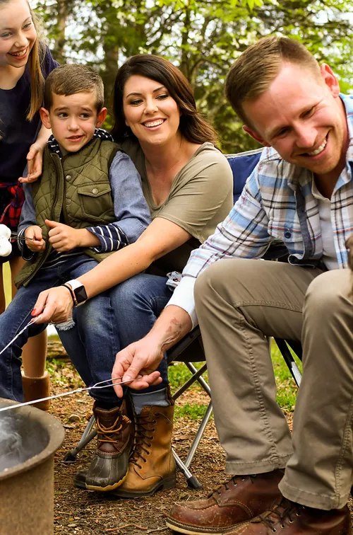 Family sitting around campfire and cooking smores