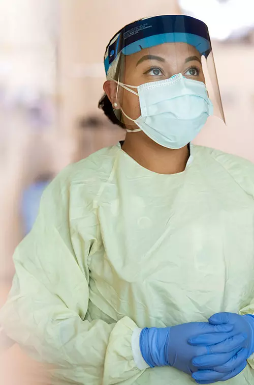 A nurse, dressed in proper personal protection equipment, stands praying.