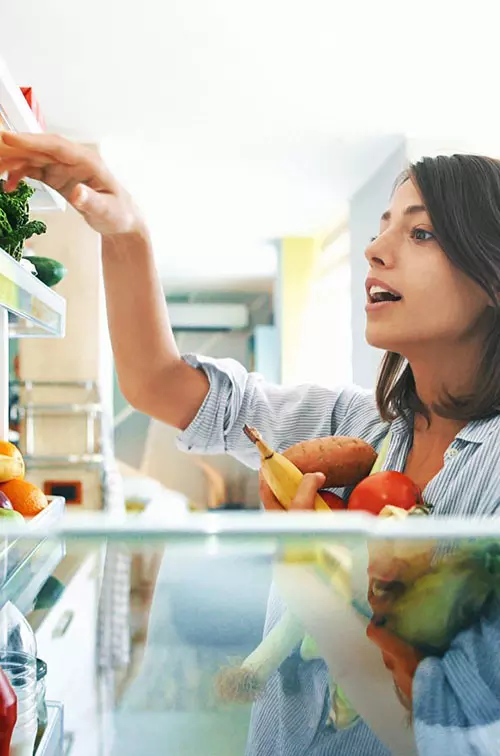 Young woman fills her arms with healthy vegetables at home