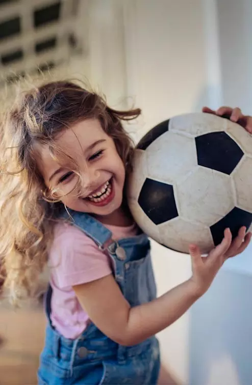 Young girl running with her family and carrying a soccer ball