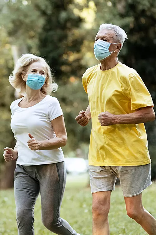 Older couple running outdoors while wearing masks.