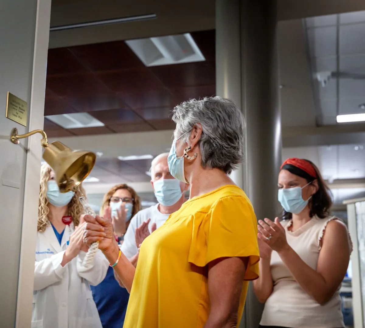 a woman ringing a cancer bell with a crowd cheering