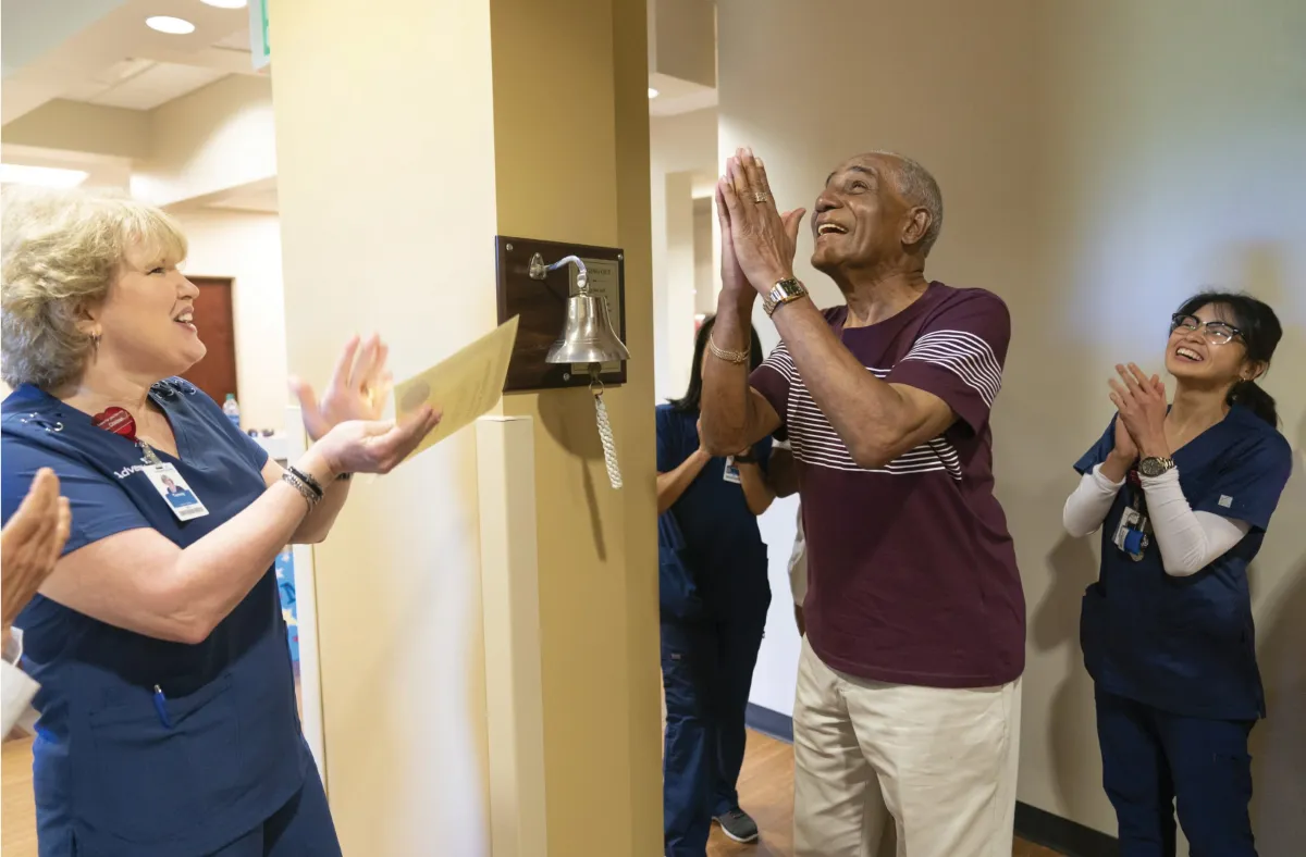 Male patient and care team celebrating after ringing cancer-free bell.