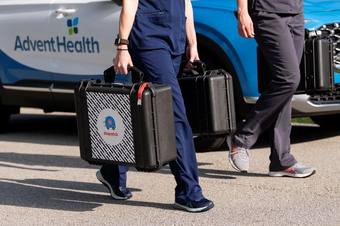 2 people in scrubs carry medical equipment in DispatchHealth cases