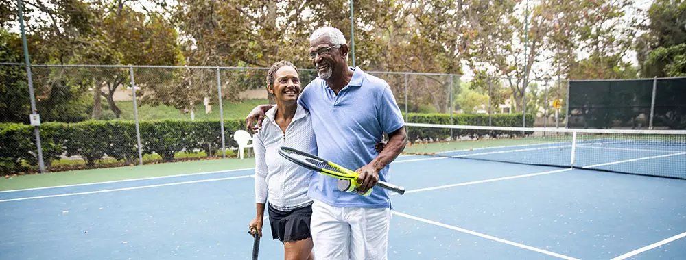 middle aged couple walks across tennis court after a game