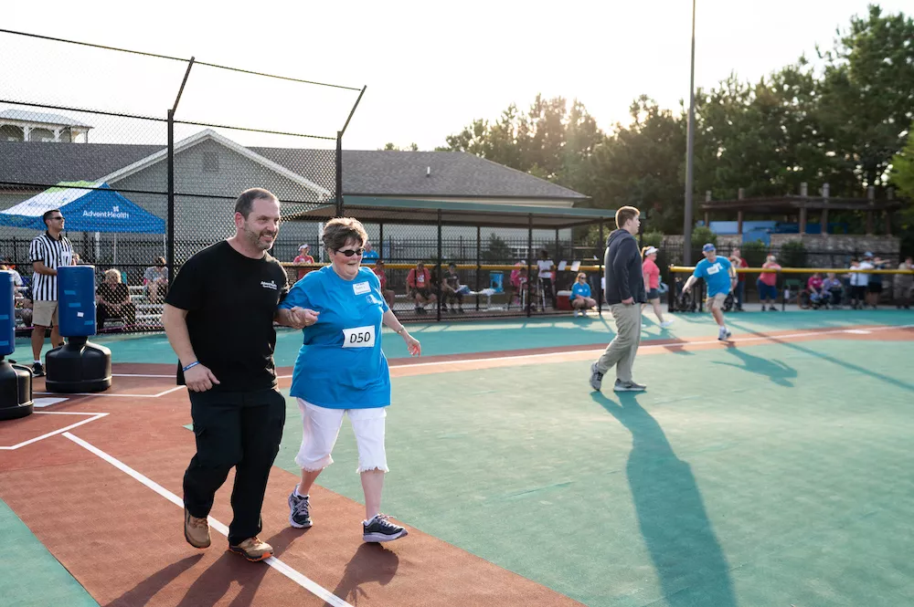 Redmond director of rehabilitation John Crowley runs with Terri Helton to first base, with student Wyatt Crowley as pitcher.